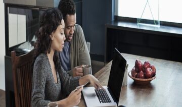 Black woman using laptop while husband drinks coffee